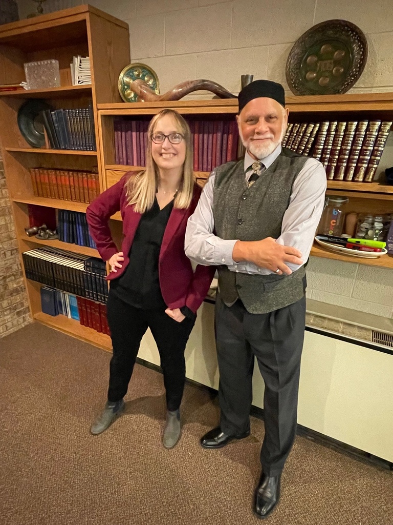 Rabbi Esther Hugenholtz (left) and Professor Motier Haskins (right) standing side by side at Hillel House in front of a row of books