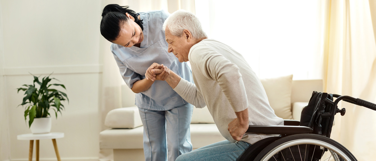 A nursing home resident being helped from a wheelchair by a nursing home worker.