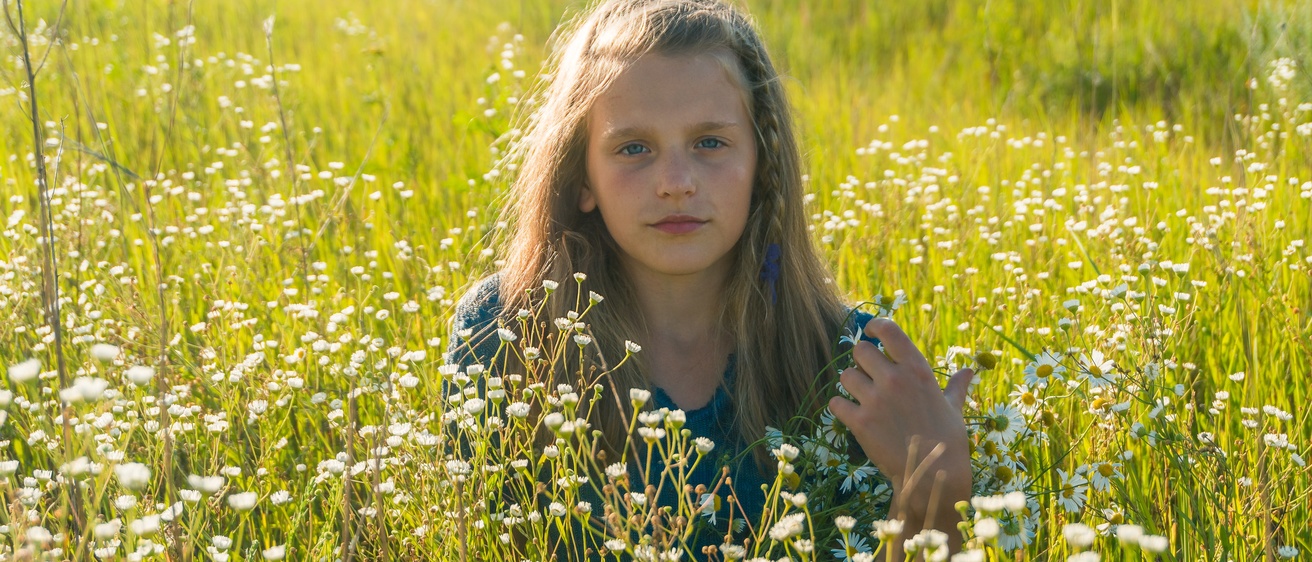 Young girl with long blonde hair sitting in a field 