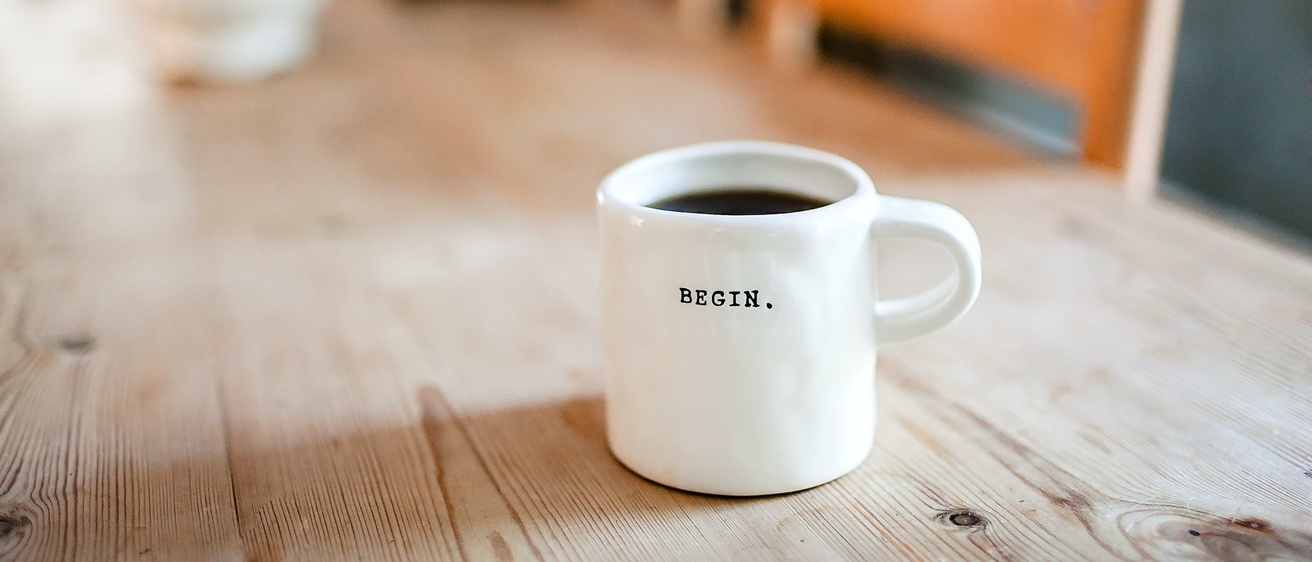 white ceramic mug on a wooden table with the word "BEGIN" printed on the side