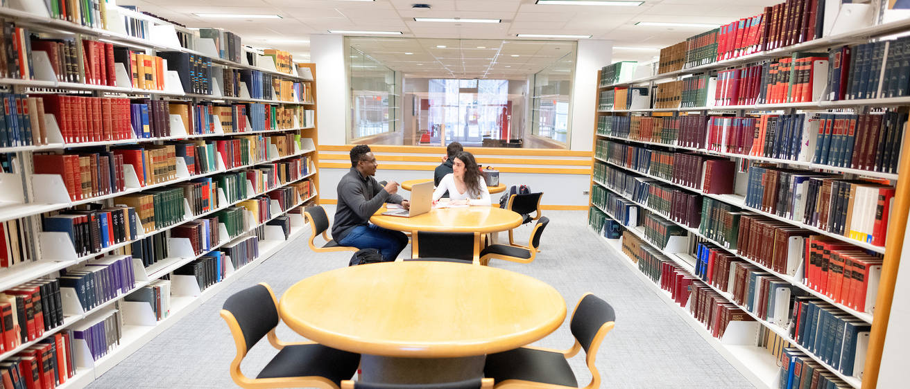 two people seated at a table engaged in conversation, in a library setting