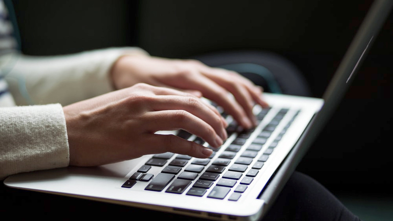 A woman's hands typing on a laptop keyboard